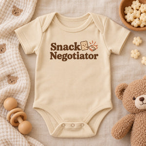 Styled flat lay of the Snack Negotiator baby bodysuit