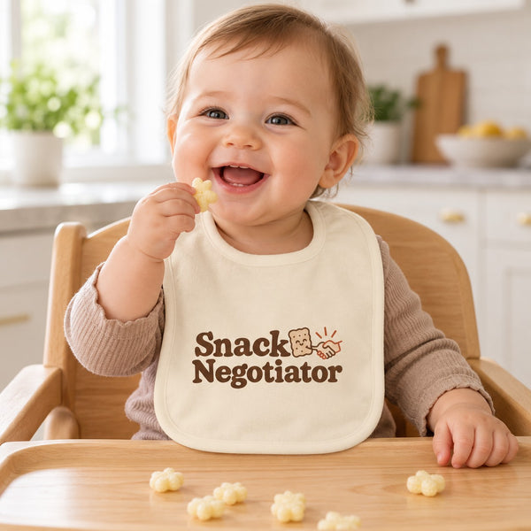 Snack Negotiator baby bib in cream, styled photo 1