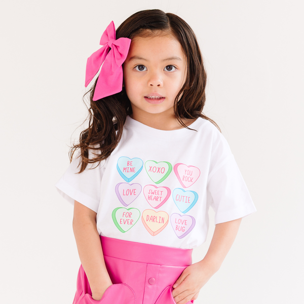 Colorful baby t-shirt with conversation hearts design, angled view showcasing playful and cute style for infants.
