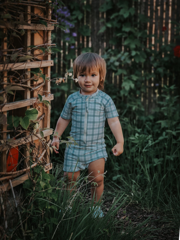 Short sleeve rashguard swimsuit in fern plaid, UPF protection, eco-friendly, angle view. Perfect for baby beach days.