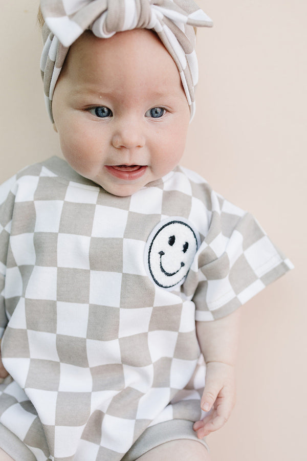 Short Sleeve Bubble Romper in Checkered Smiley Latte for babies, stylish and comfy for warm days.