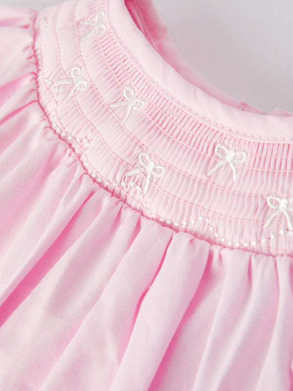 White bow smock embroidered pink romper for babies, angle view showcasing cute design and details.