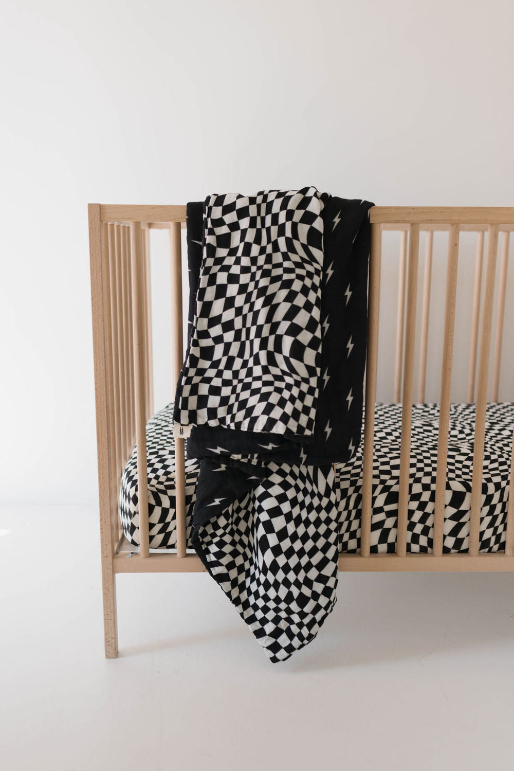 Muslin crib sheet in black and white wavy checkerboard pattern for stylish nursery decor.