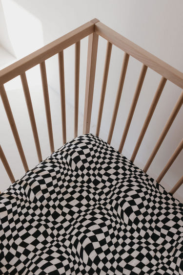 Muslin crib sheet in black and white wavy checkerboard pattern for stylish nursery decor.