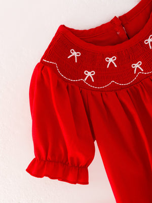 Girls red romper with bow smocking and embroidery, angle view showcasing cute design and details.