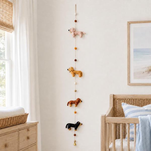 Felt dachshund garland with four colored dogs and pom bead accents hanging on a soft white nursery wall.