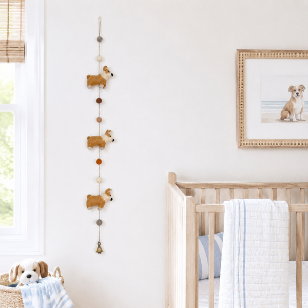 Felt corgi garland hanging on a nursery wall beside a window and a crib with blanket