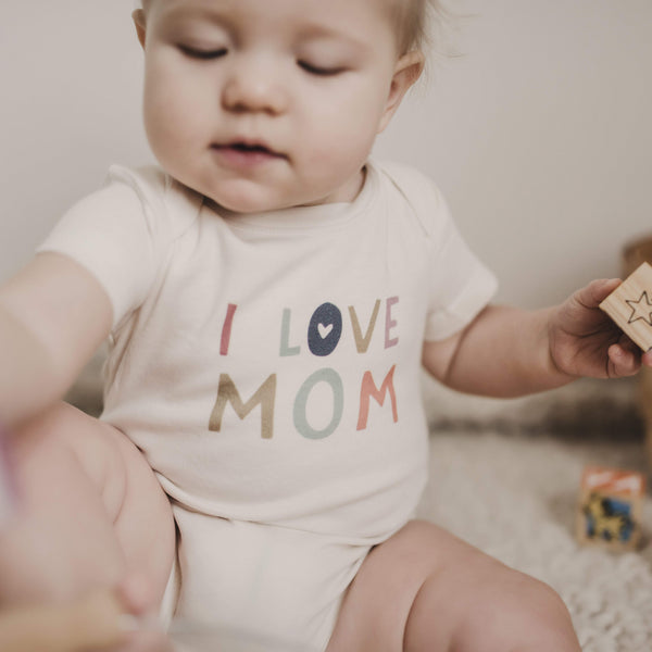 Graphic bodysuit with "Love Mom" design, short sleeves, angled view showcasing soft fabric and cute style for babies.