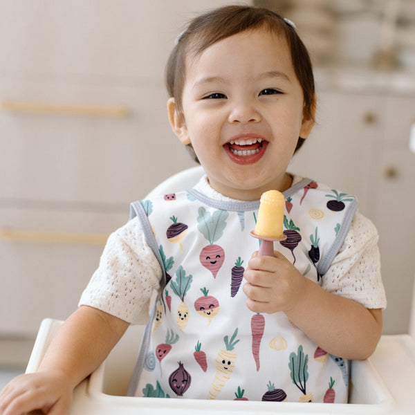 Root Veggies Bapron for babies, shown from angle 2, featuring colorful vegetable prints for mealtime fun.