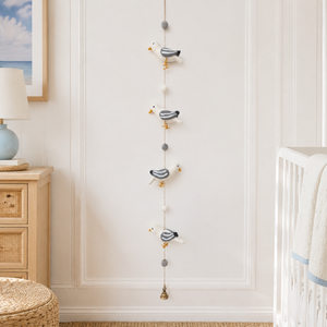 Felt seagull garland hanging on a white wall near a crib, showing four wool birds and a small bell