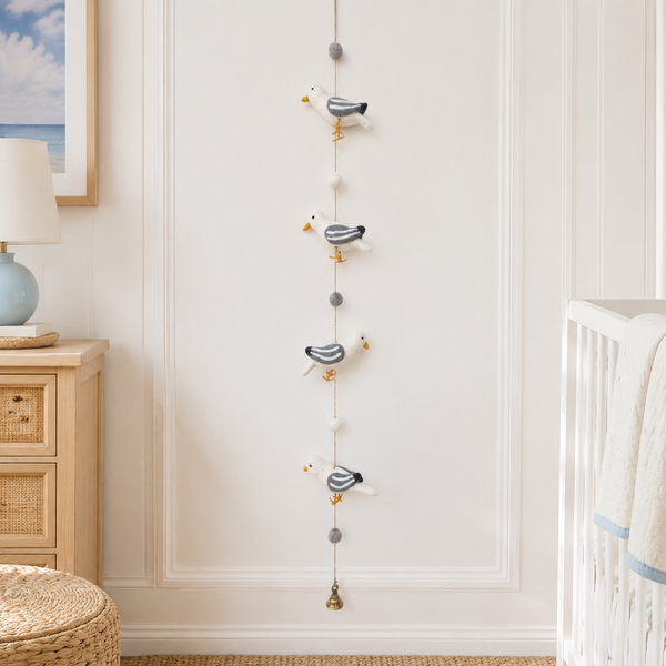Felt seagull garland hanging on a white wall near a crib, showing four wool birds and a small bell