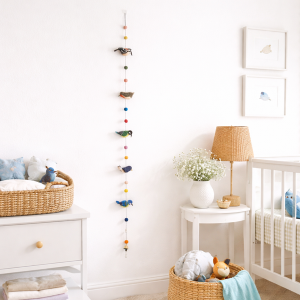 Felt bird garland displayed in a nursery beside a crib, wool birds and felt balls in view
