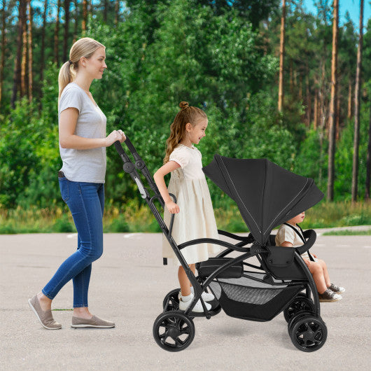 Foldable twin tandem stroller in black, featuring adjustable handlebar for sit and stand convenience.