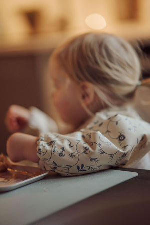 Scandi Floral Smock Bib for babies, featuring a stylish design and practical coverage, displayed at an angle.