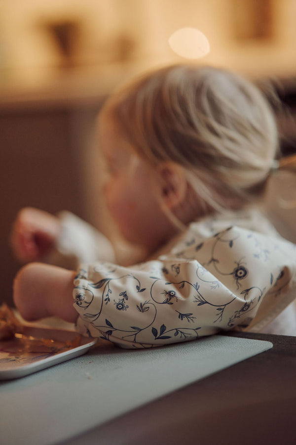 Scandi Floral Smock Bib for babies, featuring a stylish design and practical coverage, displayed at an angle.