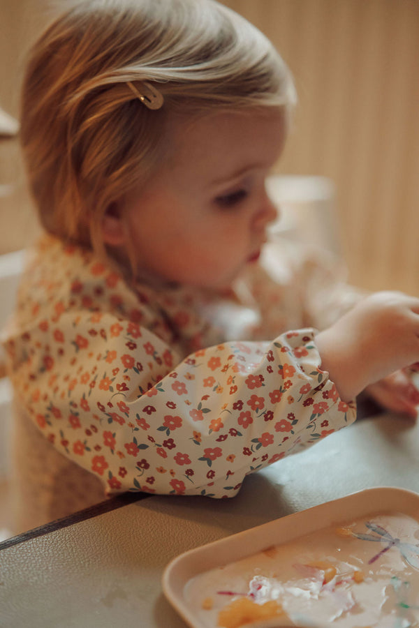 Smock Bib in Sunset Meadow design, angled view showcasing vibrant colors and practical features for feeding.