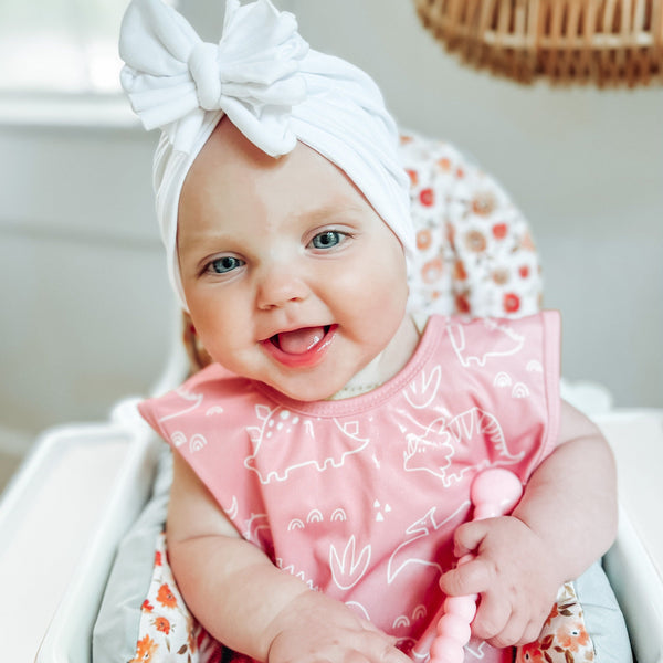 Blush Dino Friends Bapron for babies, stylish and functional, angled view showcasing its cute dinosaur design.