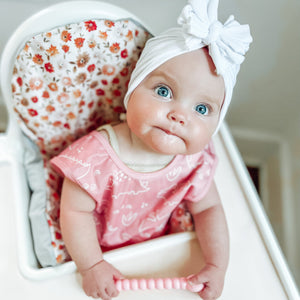 Dino Friends Blush Bapron for babies, angled view showcasing playful dinosaur design and practical bib features.