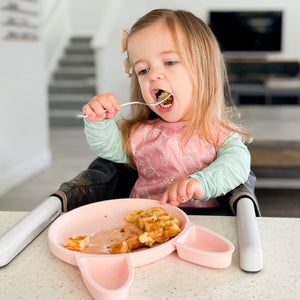 Blush Dino Friends Bapron for babies, angled view showcasing playful design and practical features.