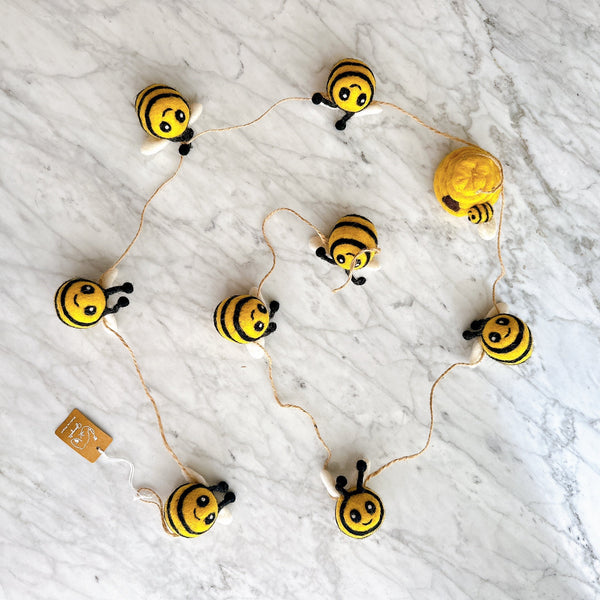 Felt bee garland laid flat on marble, showing hand-crafted wool bees and a small hive charm