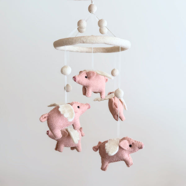 Felt flying pig baby mobile on a plain background, showing five pink pigs with cream felt wings and a felt hoop.