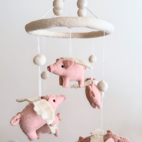 Low angle close-up of the felt pig baby mobile showing layered wool felt animals and pom pole beads.