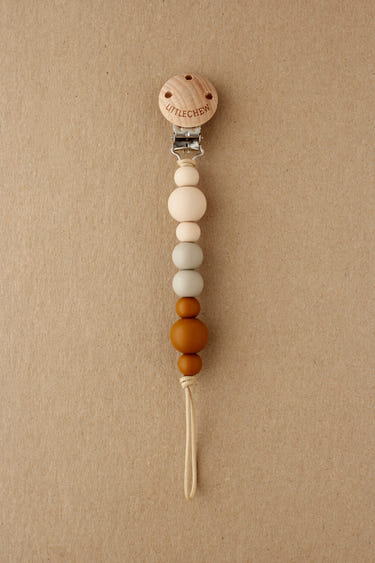 Neutral Kira pacifier clip for babies, stylish and functional accessory to keep pacifiers within reach.