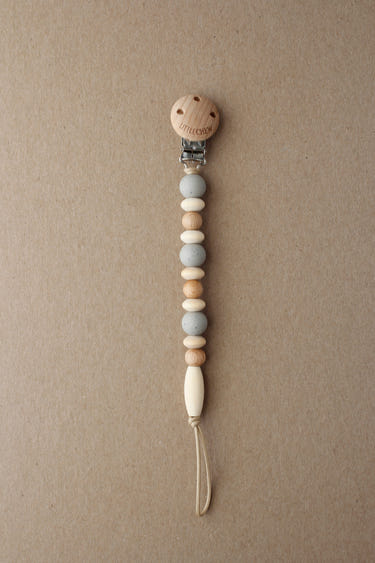 Speckled taupe Omar pacifier clip for babies, stylish and practical accessory for keeping pacifiers within reach.
