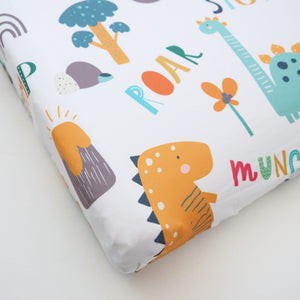 Dinoland changing pad cover for babies, featuring colorful dinosaur prints, angled view showcasing soft fabric and design.