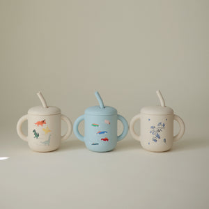 Silicone training cup with straw for babies, angled view showcasing its ergonomic design and vibrant colors.