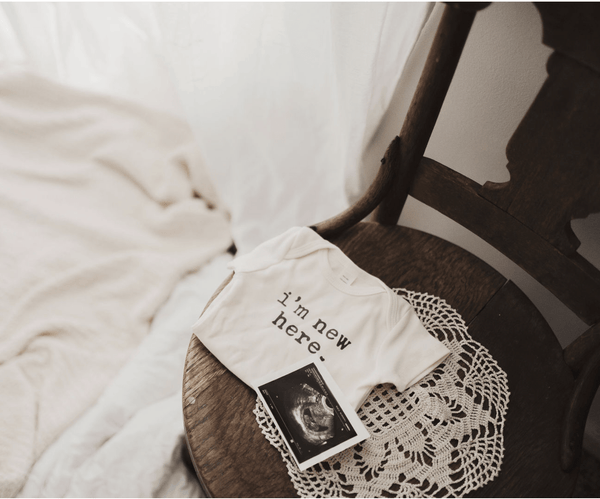 Graphic bodysuit for babies with "I'm New Here" design, short sleeves, shown from angle 3. Perfect for newborns!