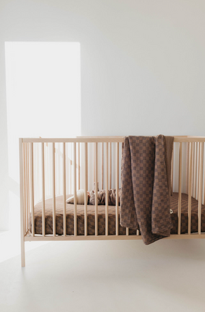 Faded brown checkerboard muslin quilt for babies, showcasing a cozy and stylish design from an angled view.