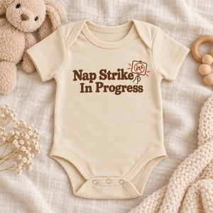 Styled flat lay of the Nap Strike In Progress baby bodysuit