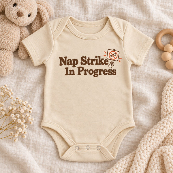 Styled flat lay of the Nap Strike In Progress baby bodysuit