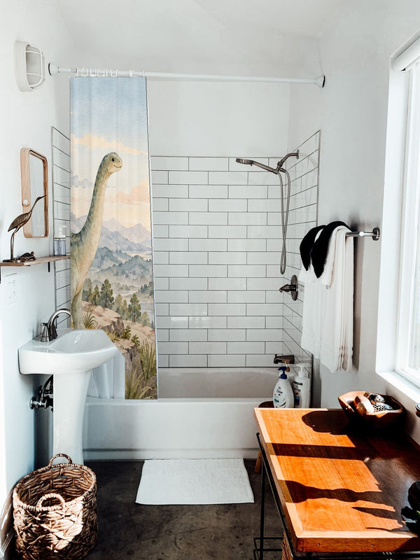 Mountain Dinosaur shower curtain hanging on the rod over a white bathtub