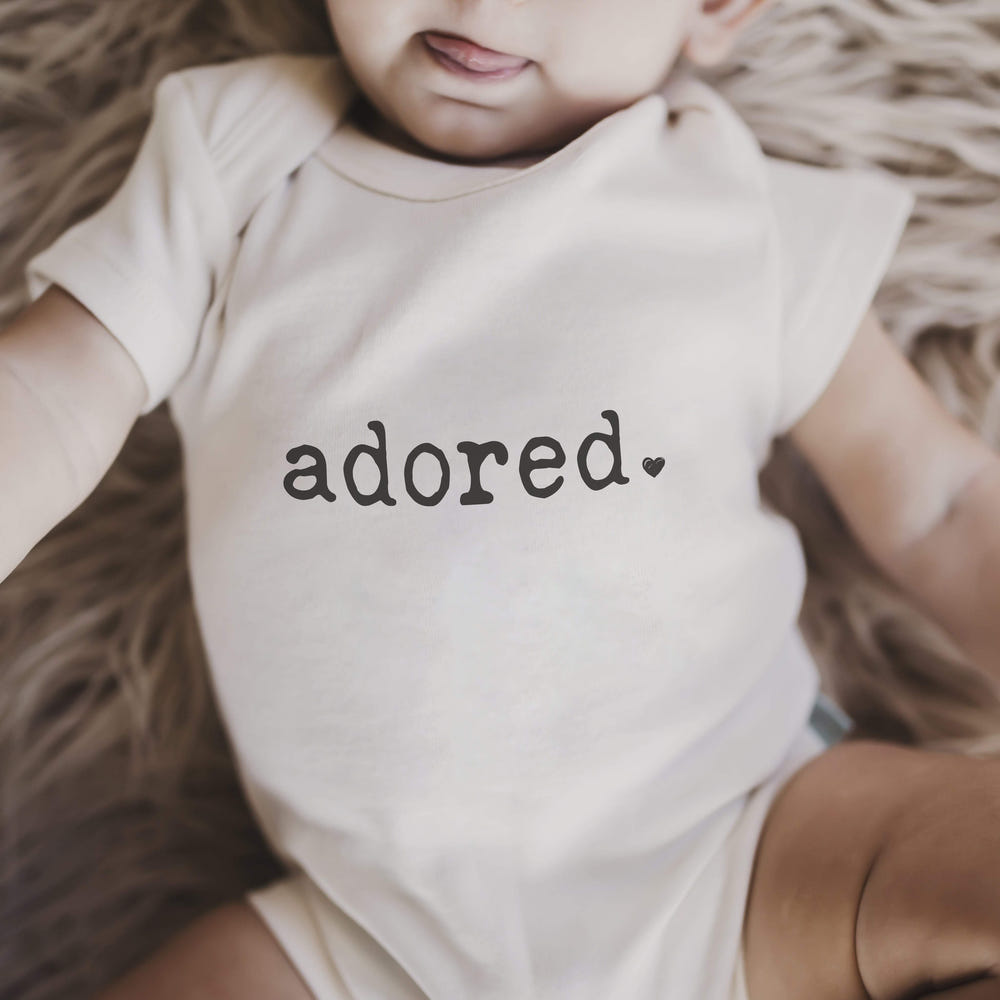 Adored short sleeve graphic bodysuit for babies, featuring a cute design and soft fabric. Perfect for everyday wear.