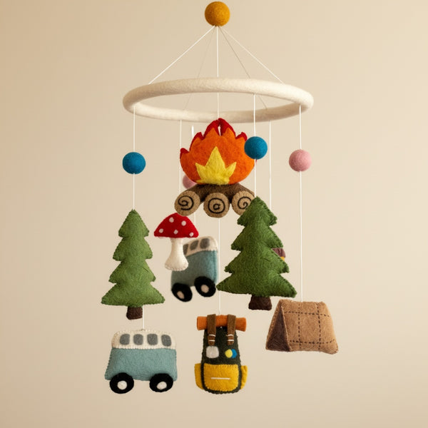 Camping felt baby mobile from a low angle against a softly blurred cream wall, warm light.