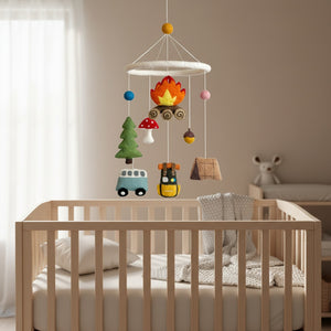 Camping felt baby mobile hanging above a light wood crib in a calm, sunlit nursery.