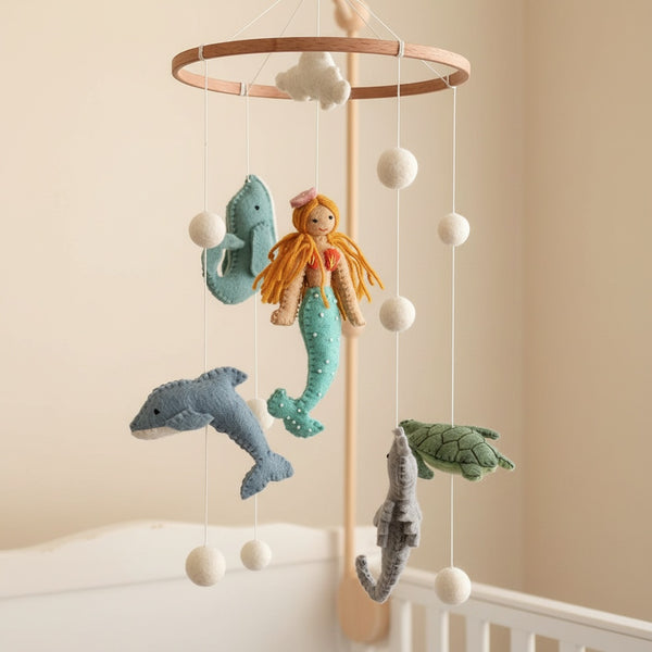 Close-up of the mermaid baby mobile's felt figures from a low angle against a cream wall