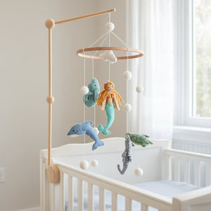 Mermaid baby mobile hanging above a light wood crib in a bright, softly lit nursery corner