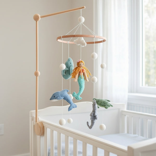 Mermaid baby mobile hanging above a light wood crib in a bright, softly lit nursery corner