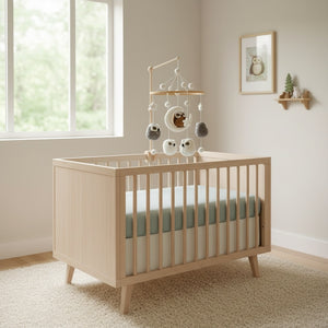 Owl felt baby mobile hanging over a light wood crib in a calm, bright nursery