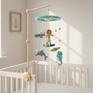 Felt surfer boy and ocean creatures mobile hanging above a light wood crib in a bright nursery