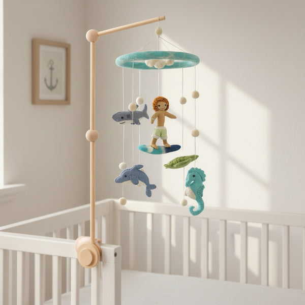 Felt surfer boy and ocean creatures mobile hanging above a light wood crib in a bright nursery