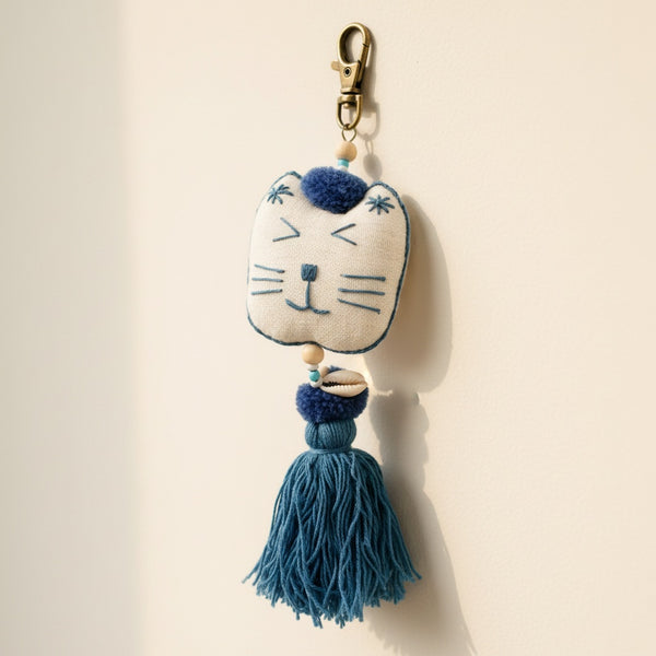 Close-up of the embroidered cat face, blue pompom, and shell beads on the cotton keychain