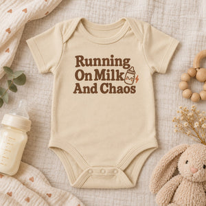 Styled flat lay of the Running On Milk And Chaos baby bodysuit