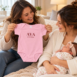 Aunt holding up the pink embroidered Ava bodysuit for her newborn niece