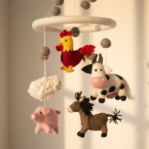 Low angle close-up of the wool felt farm animal baby mobile against a blurred cream wall.