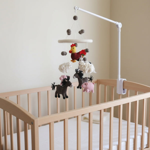 Wool felt farmland animal baby mobile hanging above a light wood crib in a calm nursery.