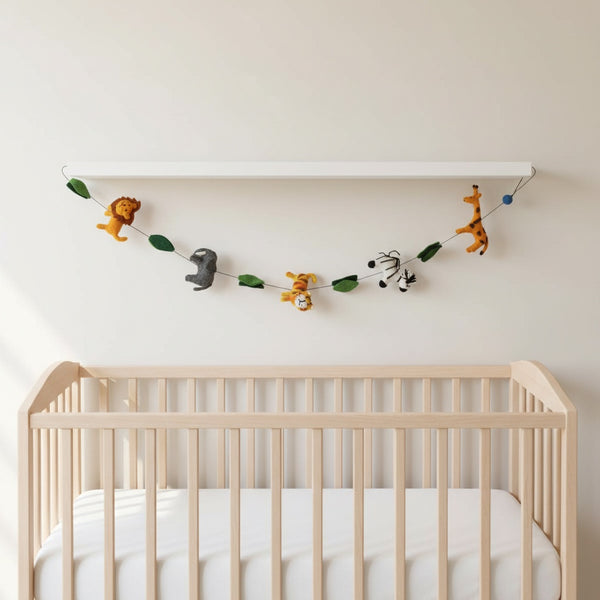 This felt safari animal garland hanging along a nursery wall near a crib, filled with soft daylight.